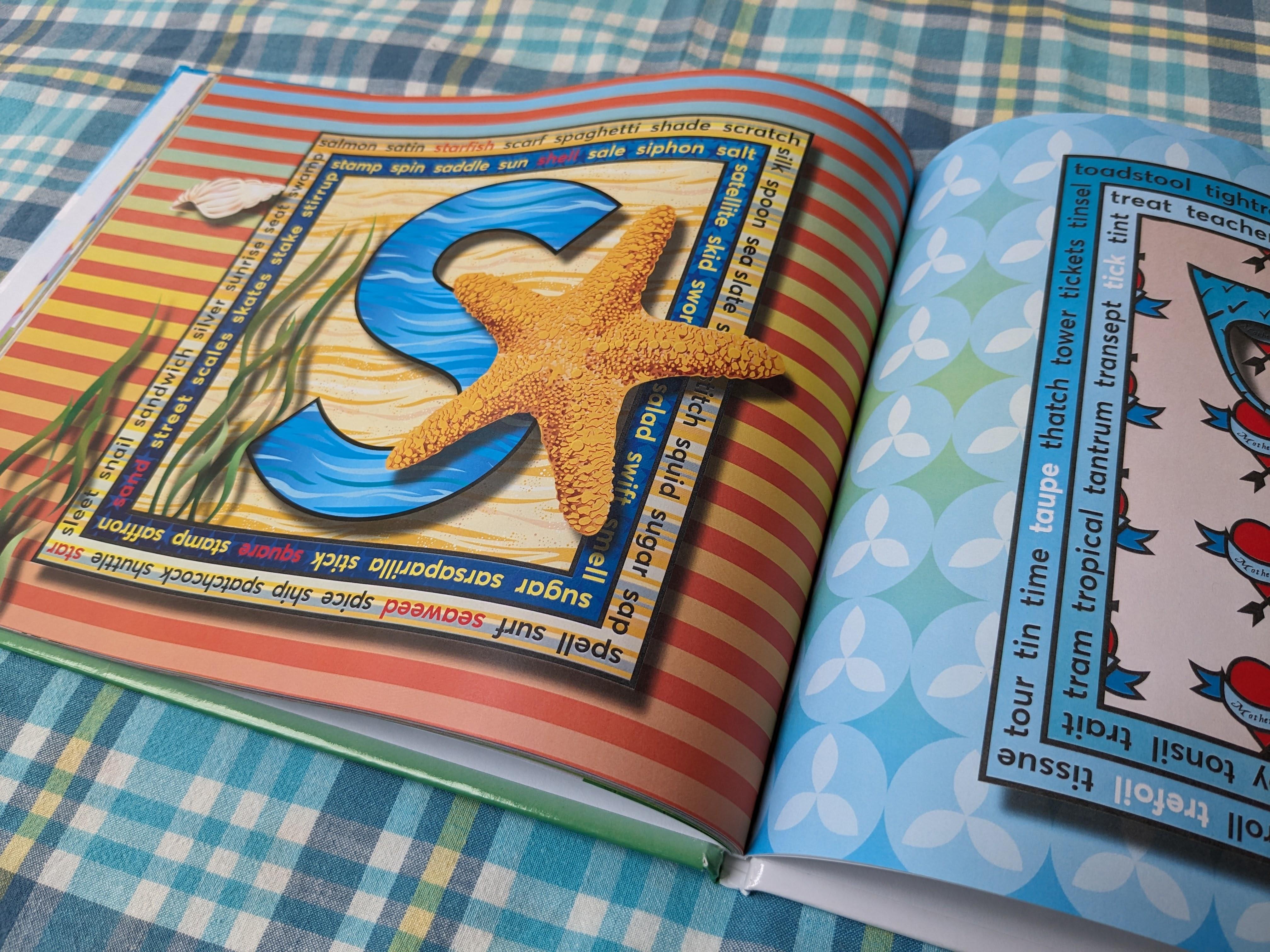 Photograph of the open alphabet book lying flat on a checked surface. The left page features a blue letter S with a large orange textured starfish resting on a sandy background.